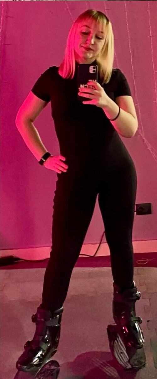 Person wearing a black outfit with reflective shoes on a pink background