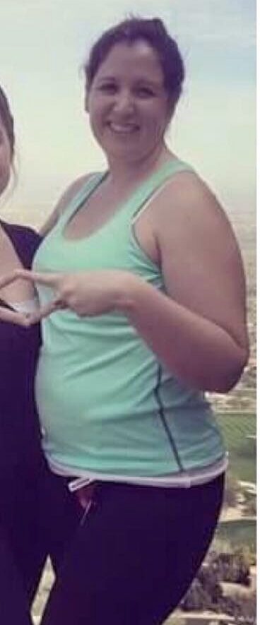 Woman in a light green tank top and purple pants standing outdoors with a scenic background.