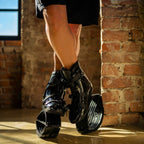 Close-up of a person standing with crossed legs while wearing Fit Boots Rebound Boots indoors.