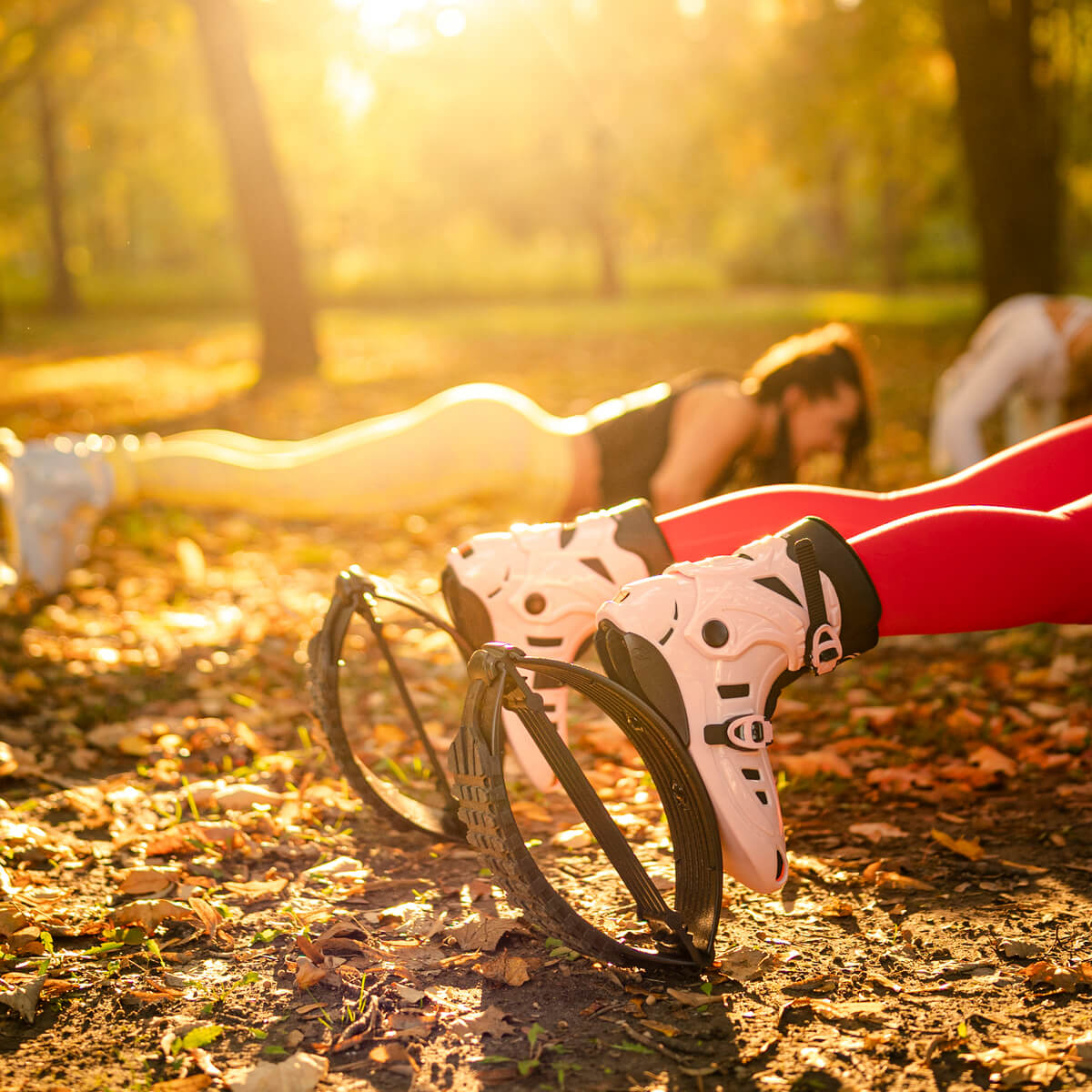 Close-up of people doing planks outdoors while wearing Fit Boots Rebound Boots in pink