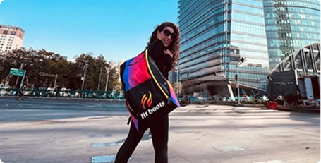 Person holding a colorful backpack with 'Fit Board' branding in an urban setting.