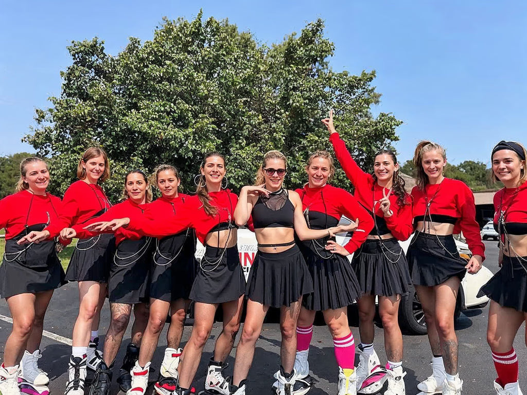 Group of women in red tops and black skirts posing outdoors.