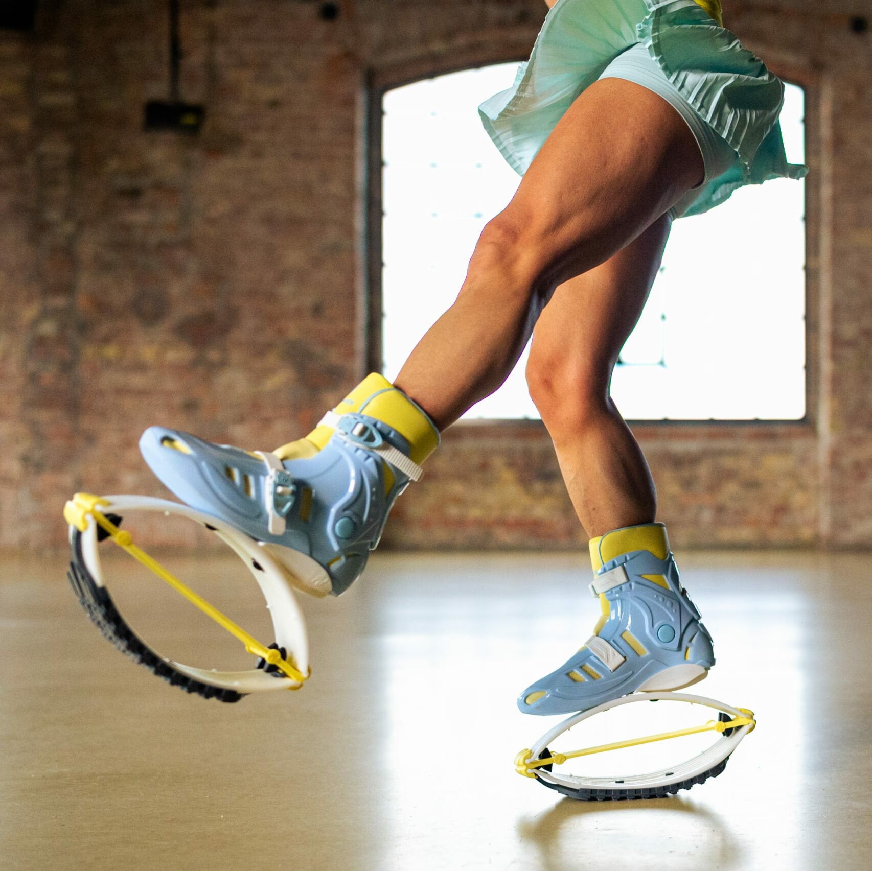 Person using spring shoes in a room with brick walls and a large window.