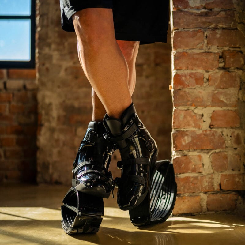 Primer plano de una persona de pie con las piernas cruzadas mientras lleva puestas las botas de rebote Fit Boots en interiores.