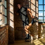 Homme adossé à un mur de briques, posant et s'étirant tout en portant des bottes de rebond Fit Boots à l'intérieur.